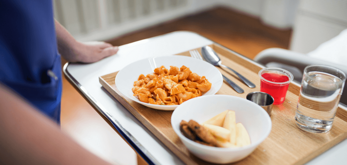 Hospital employee placing meal tray on bedside table